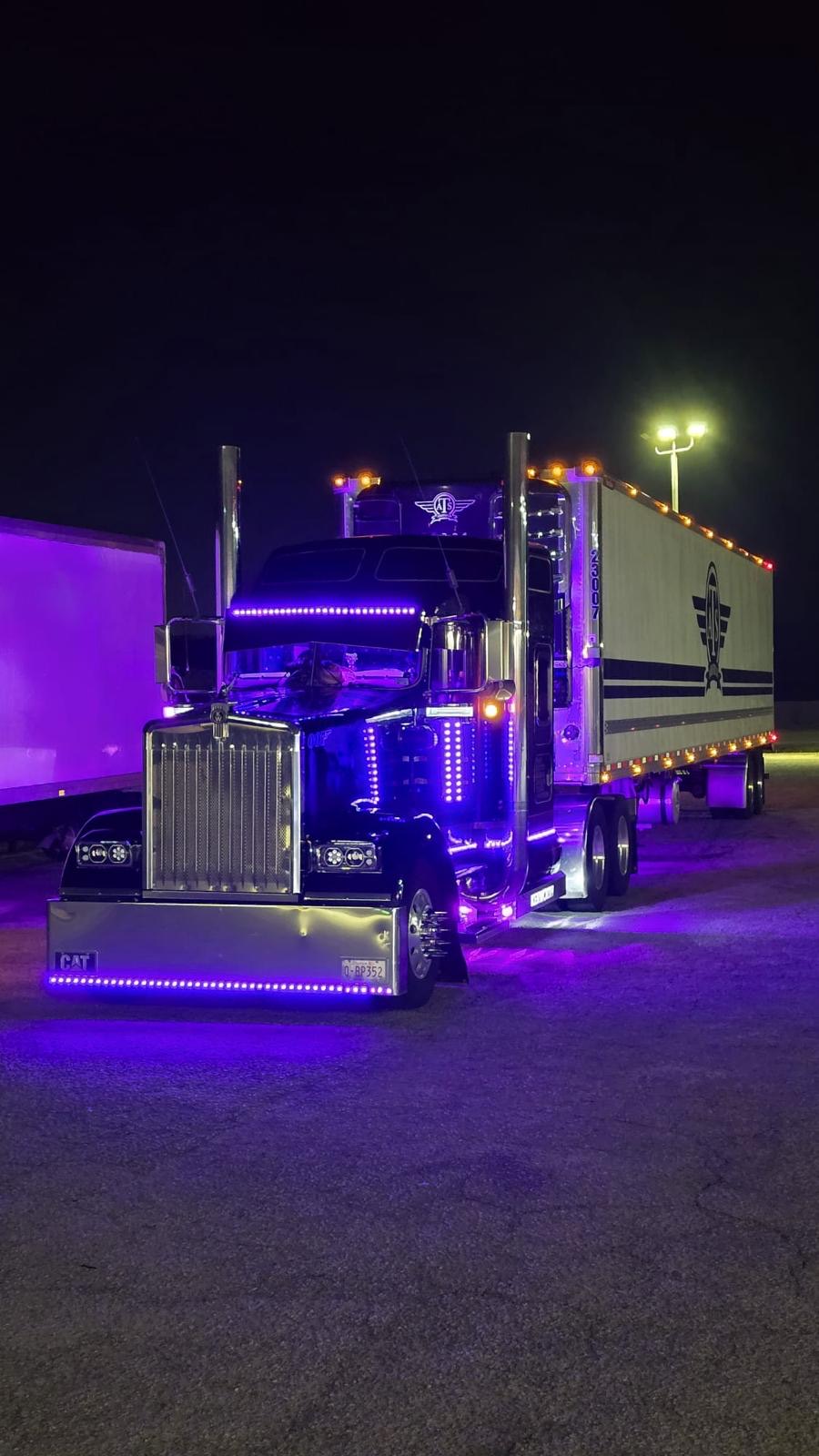 A black Kenworth tractor with chrome and purple LED accents photographed at night