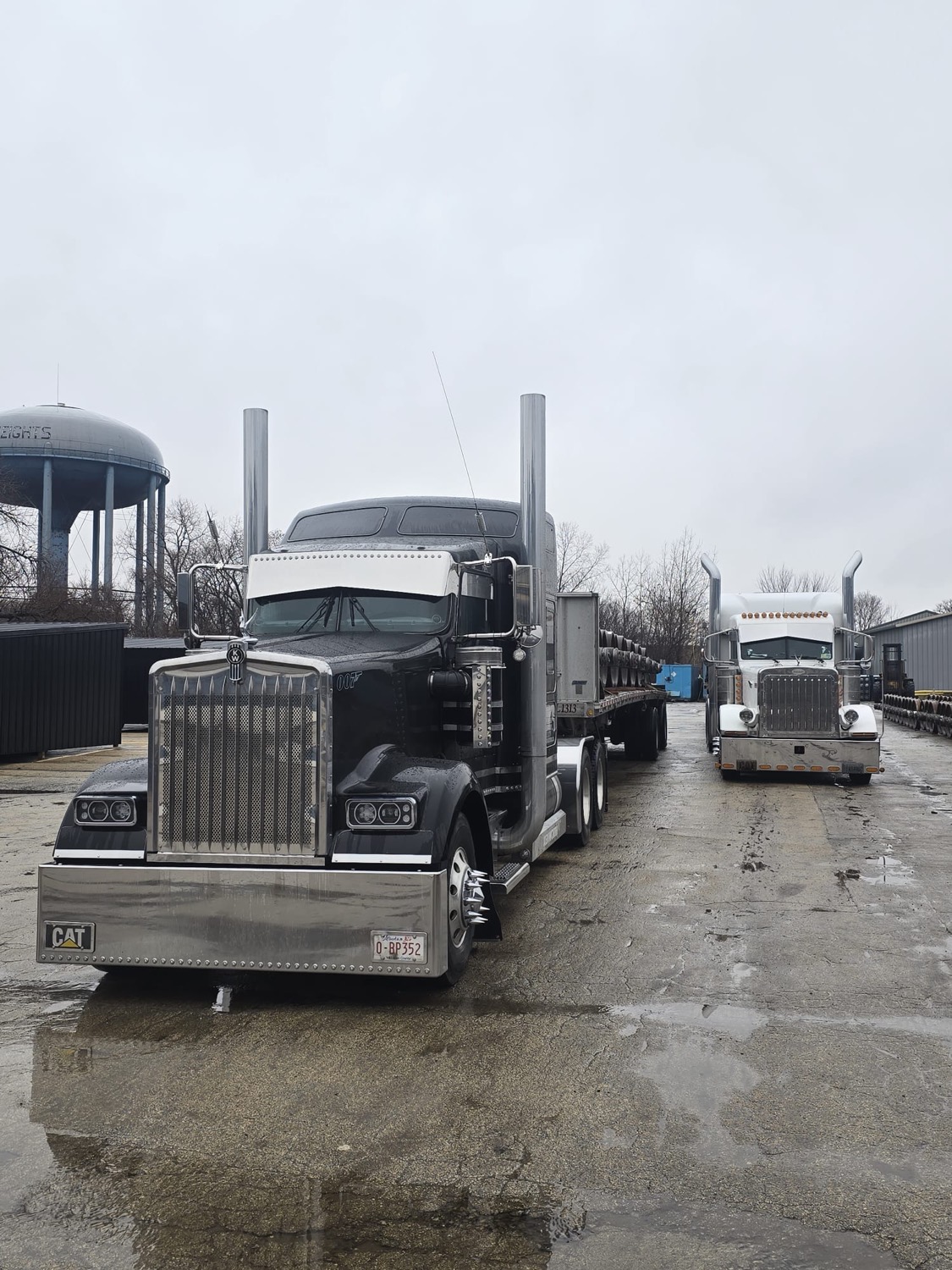 Black and white Kenworth flatbed tractors parked at the yard with CAT bumpers