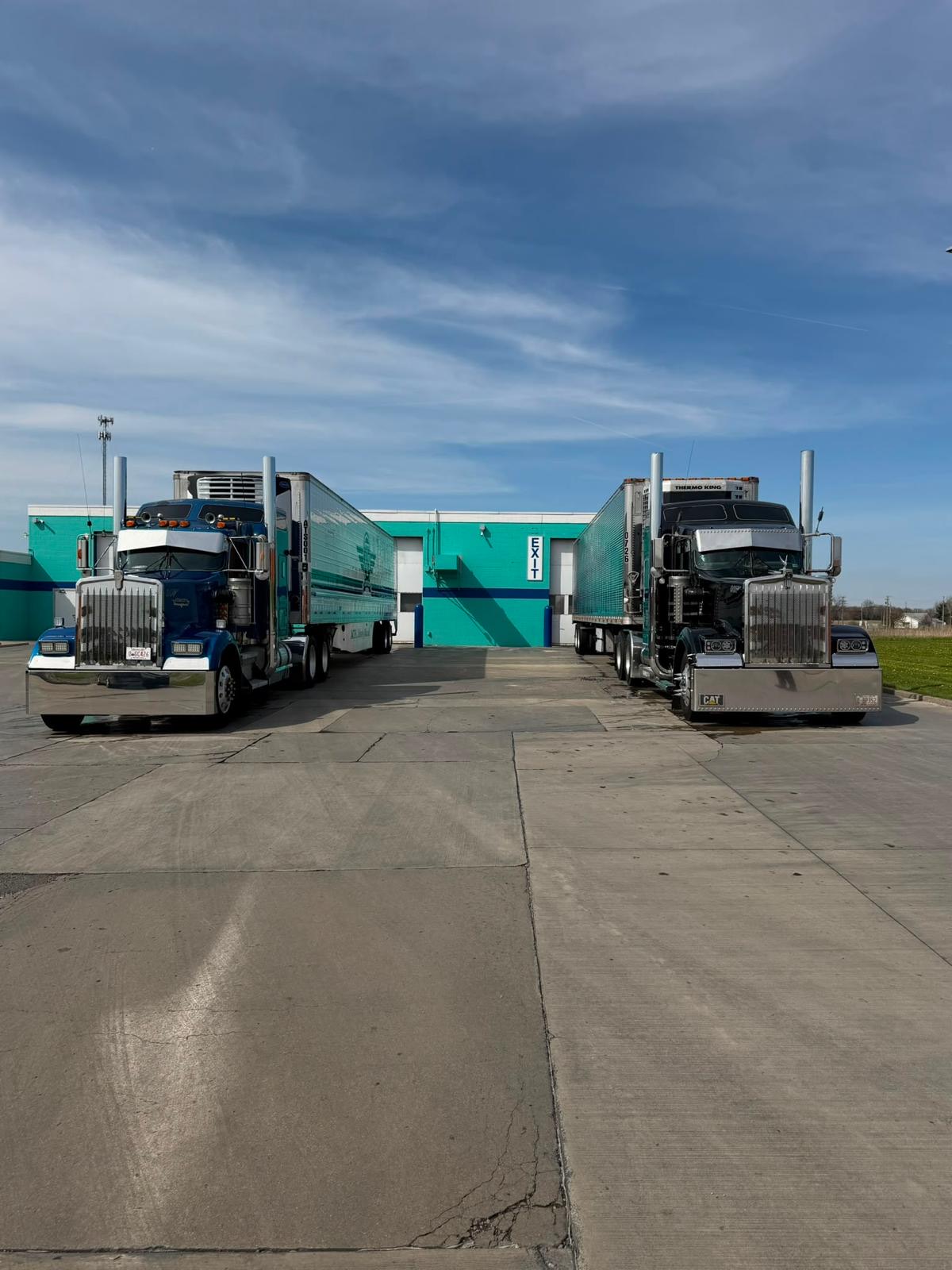 Two chrome Airfield Trucking tractors at a warehouse loading dock in daylight