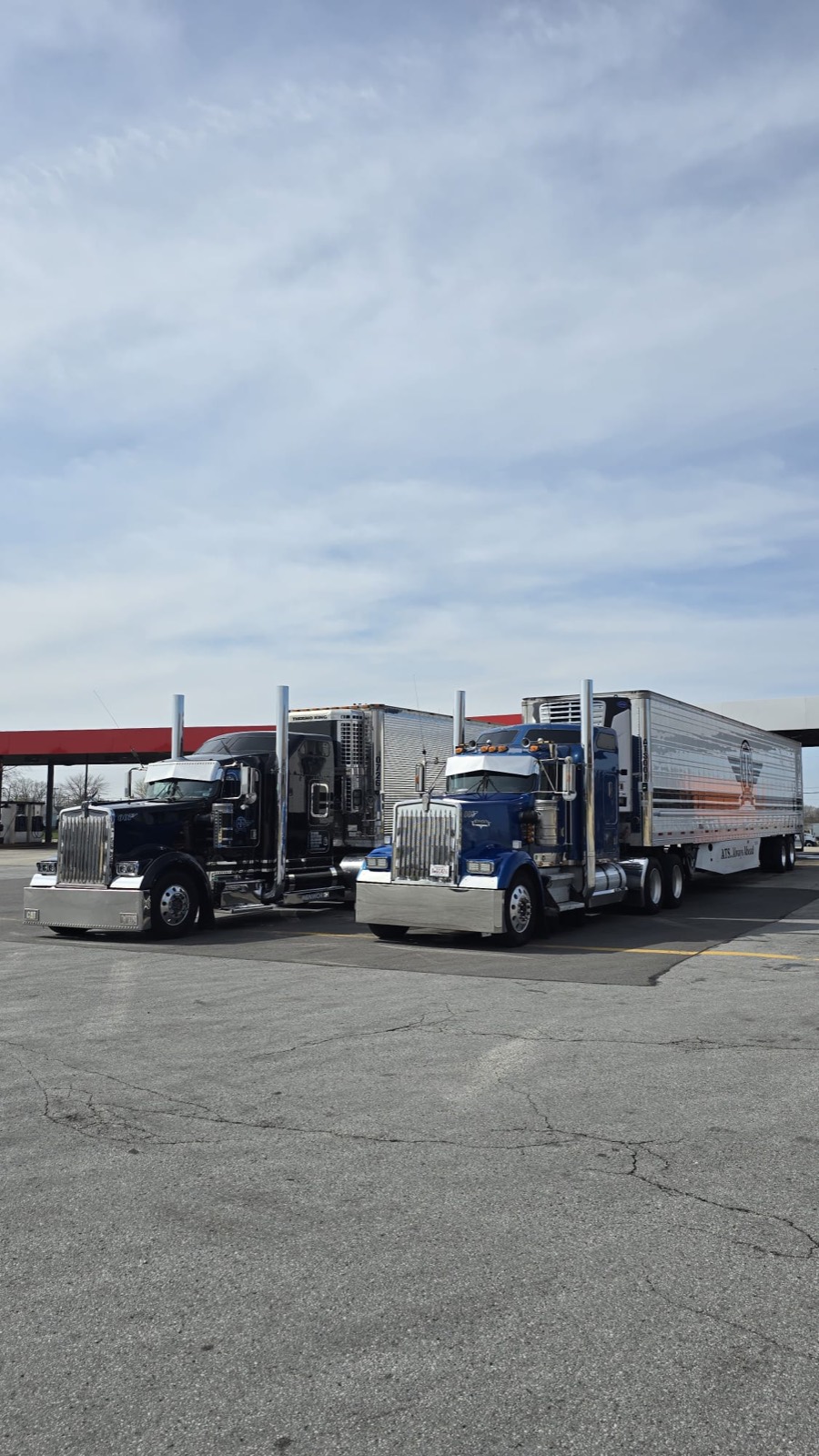 A Peterbilt and a blue Kenworth tractor fuelling at a fuel island