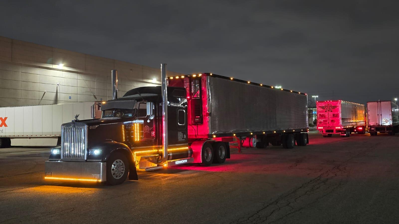 Airfield Trucking black Kenworth W900 with a reefer trailer at a warehouse dock at night